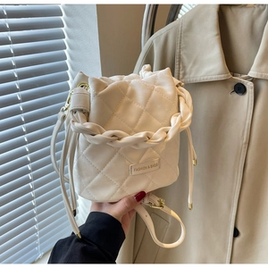 Detail der cremefarbenen gesteppten Beuteltasche mit geflochtenem Griff und Goldplakette