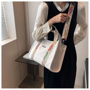 Detail of white canvas tote bag featuring floral embroidery on a wide shoulder strap