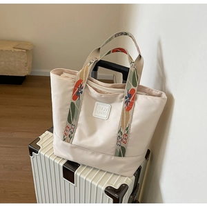 Detail of off-white tote bag with floral printed handles resting on a white suitcase