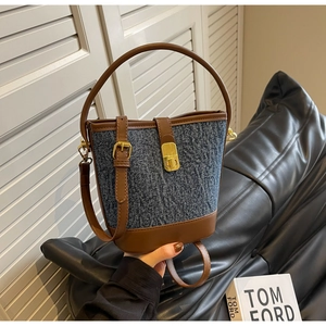 Detail of blue denim and brown leather bucket bag with golden metallic clasp