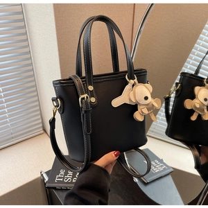 Detail of black leather bucket bag with contrast stitching and bear charm