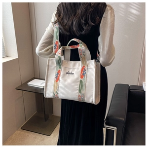 Detail of floral embroidered shoulder strap on off-white canvas tote bag worn by model