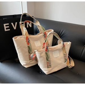 Detail view of beige canvas tote bags with colorful floral handles on a leather sofa