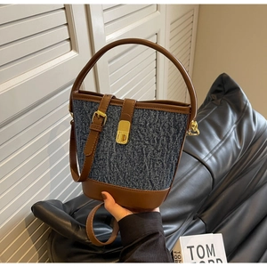 Detail of denim bucket bag with leather trim and gold buckle in minimalist studio setting
