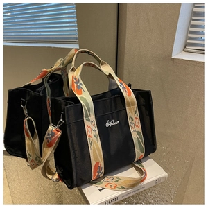 Detail of black nylon tote bag with floral pattern strap and white letter embroidery