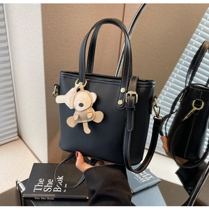 Detail of black bucket bag with white contrast stitching and a cute bear charm pendant