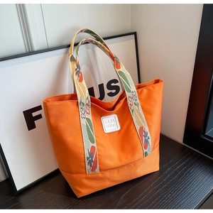 Close-up of orange canvas tote bag with floral embroidered handles and logo patch