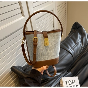 Detail of a textured bucket bag with brown leather trim and golden metal turn-lock