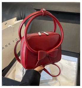 Detailed view of red bow handbag in premium black gift box with gold circular handle