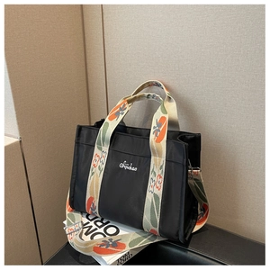 Detail of black canvas tote bag featuring floral embroidered wide strap and logo
