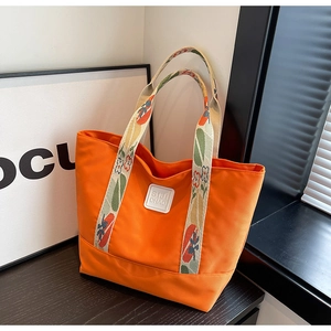 Detail of orange tote bag with floral strap and SIJI CHAO logo on wooden table