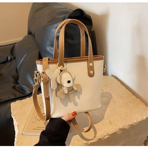 Detail of two-tone bucket bag with leather bear charm on stone pedestal background