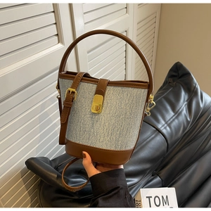 Detail of blue denim bucket bag featuring brown leather trim and gold metal lock hardware
