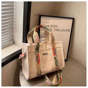 Detail of off-white canvas tote bag featuring colorful floral embroidery on the wide strap