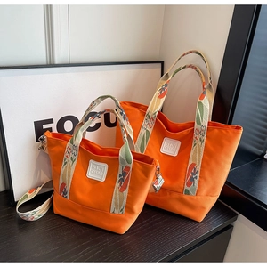 Detail of orange nylon tote bag set with floral straps and SIJI CHAO logo branding