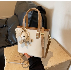 Detail of bicolor bucket bag with cute bear charm and gold-tone hardware on stone base