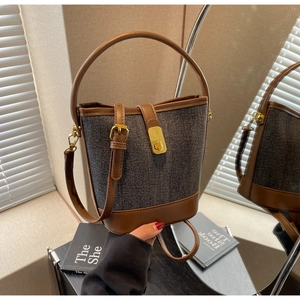 Detail of grey denim bucket bag with brown leather trim and golden metal swivel lock