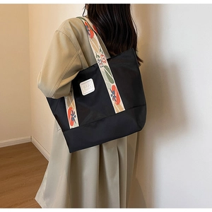 Detail of black canvas tote bag featuring floral embroidered strap and white logo patch