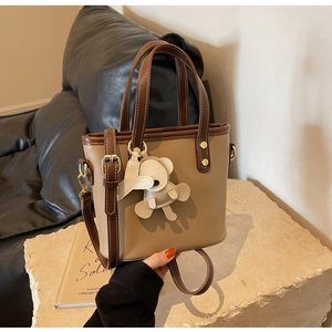 Detail of khaki bucket bag with brown trim, gold hardware and a cute bear charm