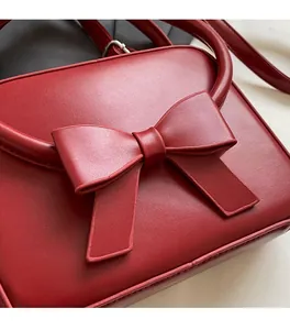 Detail of a dark red matte leather handbag with a large decorative bow and neat stitching