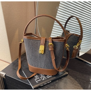 Detail of denim and brown leather bucket bag with gold clasp and top handle on wood