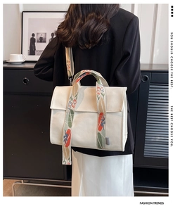 Detail of white canvas tote bag featuring a colorful embroidered wide crossbody strap