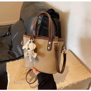 Detail of khaki bucket bag with brown trim and cute cream bear pendant on stone base