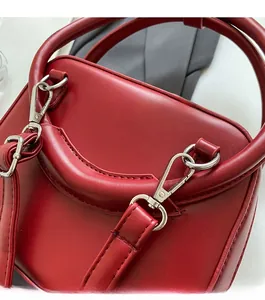 Close-up of bright red handbag with silver metal D-rings and detachable shoulder strap