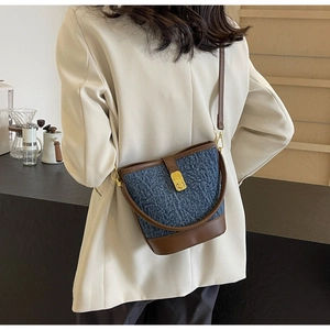 Macro detail of blue denim bucket bag with brown leather trim and golden metal clasp