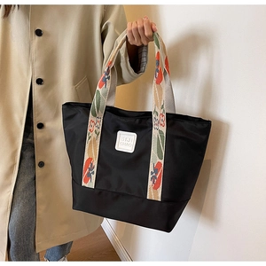 Detail of black canvas tote bag with floral woven handle and branded leather tag