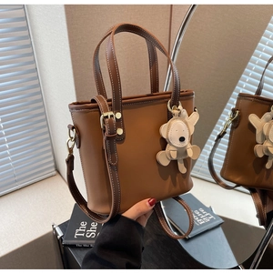 Brown leather bucket bag with white stitching detail and cute bear charm accessory