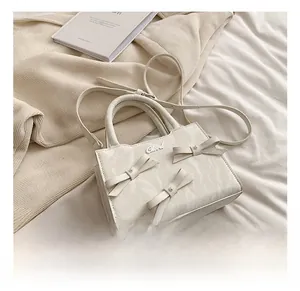 Detail einer cremeweißen Handtasche mit Schleifen-Deko und silbernem Chord-Metalllogo