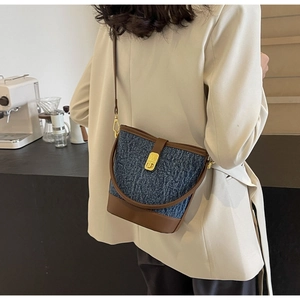 Detail of denim and brown leather bucket bag with gold clasp shown on model
