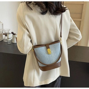 Detail of blue denim bucket bag featuring brown leather trim and golden twist lock