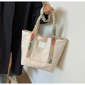 Detail of beige nylon tote bag featuring colorful floral shoulder straps and brand logo