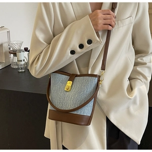 Blue denim bucket bag with brown leather trim shown on a model in a beige suit
