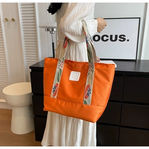 Detailed view of an orange canvas tote bag featuring embroidered floral shoulder straps