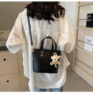 Detail of black bucket bag featuring white contrast stitching and a cute bear pendant