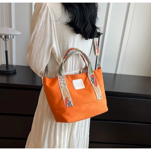 Detail of orange canvas tote with floral patterned straps and adjustable metal hardware