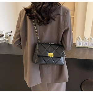 Quilted black crossbody bag with gold chain strap shown on model in a modern cafe