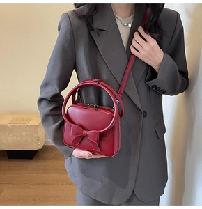 Detail of red crossbody bag with bow decoration and round handle worn by a model