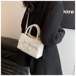 Detail einer weißen Plissee-Handtasche mit Schleifen und Perlen zum schwarzen Oversize-Blazer