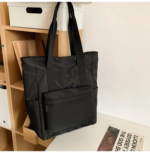 Detail of black nylon tote bag with large front zipper pocket and logo on wooden stand