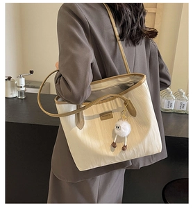 Close-up of off-white tote bag with brown leather trim and a cute plush charm accessory