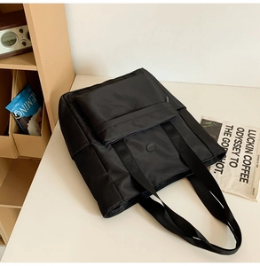 Close-up of black nylon tote bag with wide shoulder straps and front flap pocket