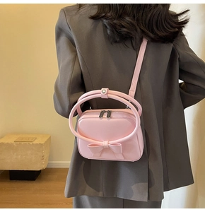 Detail of pink matte handbag with bow and silver metal hardware on a grey blazer
