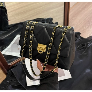 Detail of black quilted leather shoulder bag with gold square clasp and chain strap