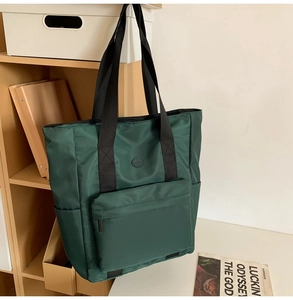 Detail of dark green nylon tote bag featuring durable black straps and zipper front pocket