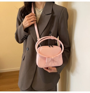 Pink PU leather handbag with a large 3D bow and round handles, worn as a crossbody bag