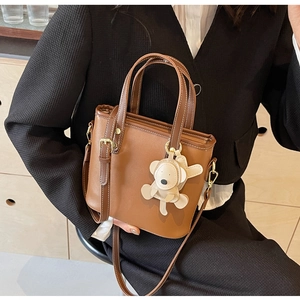 Detailed view of a brown leather bucket bag featuring white contrast stitching and bear charm